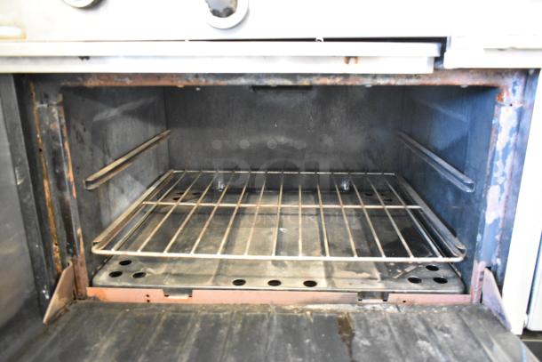 Garland metal commercial 2-section flat top gas griddle with ovens, over shelf, and backsplash. Moderate wear visible inside oven.