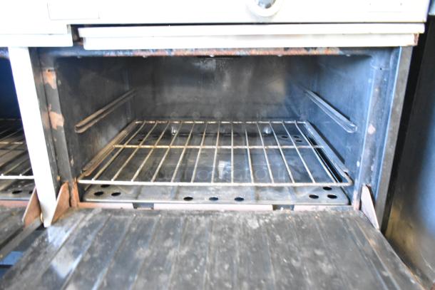 Garland metal commercial gas griddle with two sections, two ovens, over shelf, and backsplash, shown interior view. Signs of wear.