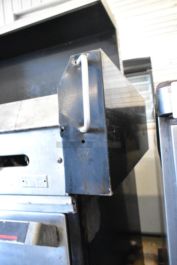 Garland metal commercial gas-powered griddle with two sections, featuring double ovens, over shelf, and backsplash. Visible wear.