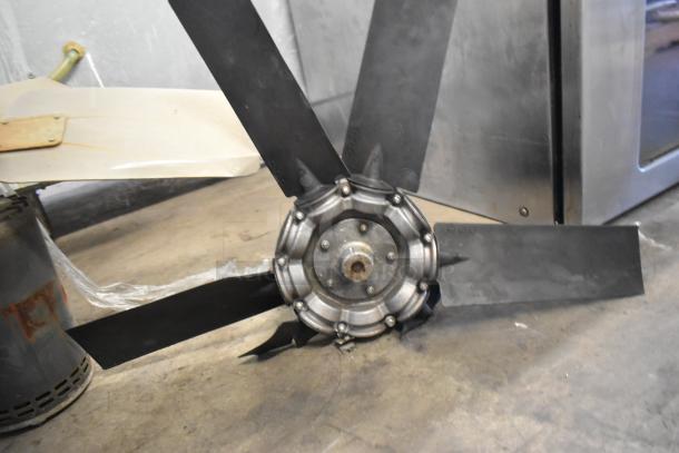 Two industrial fan blades on concrete floor, showing a metal hub and black blades. Condition appears used.