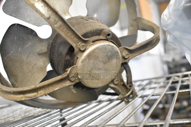 Two fan motors, including US Motors EC5472FP, shown with visible wear and metal blades on a wire shelf.