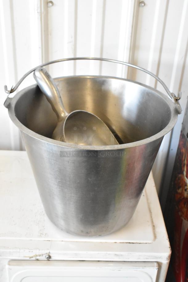 Stainless steel bucket and scoop, lightly worn, resting on a white surface.
