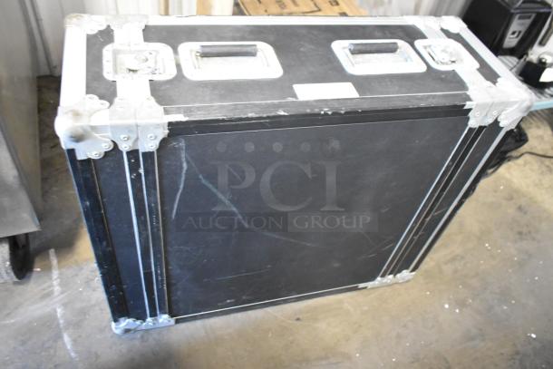 Large black equipment case with metal reinforcements and handles, showing scuff marks and a latch, part of auction lot.