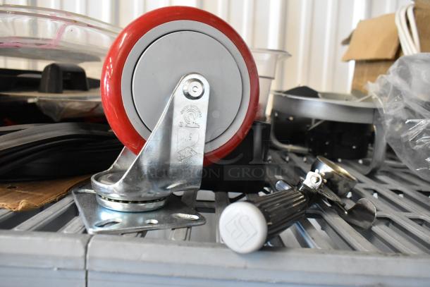 Auction lot with commercial caster featuring a red wheel, flared coupe glass, and various seals on metal shelving.