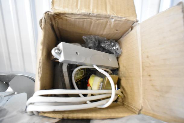 Box of assorted items including commercial casters and a flared coupe glass, some components wrapped in plastic, various seals visible.