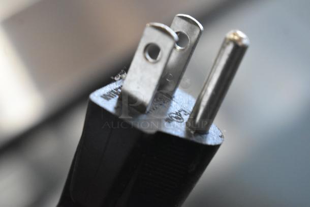 Close-up of a plug for a 2023 Magic Mill MHPE905 Electric Hot Plate, 120 volts, 1 phase, showing prongs and part of the cord.