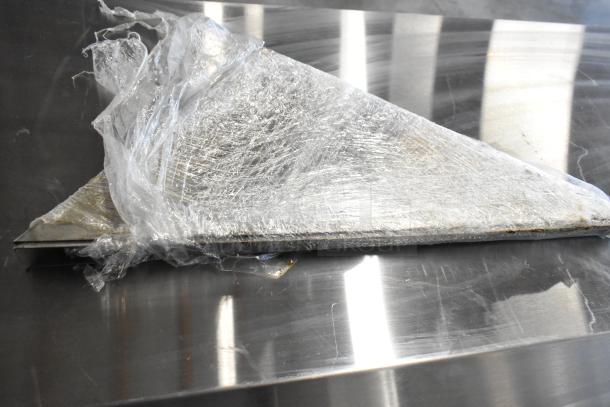 Packaged metal brackets wrapped in clear plastic on a shiny metal surface. Condition appears new, packaging intact.