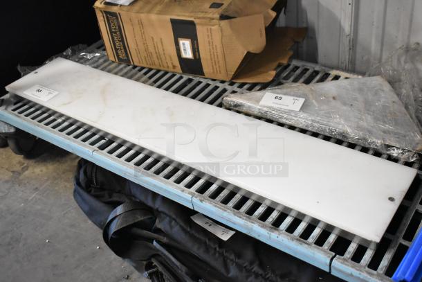 White cutting board, rectangular, with slight wear. Placed on metal shelving unit. Auction tag "68" visible.