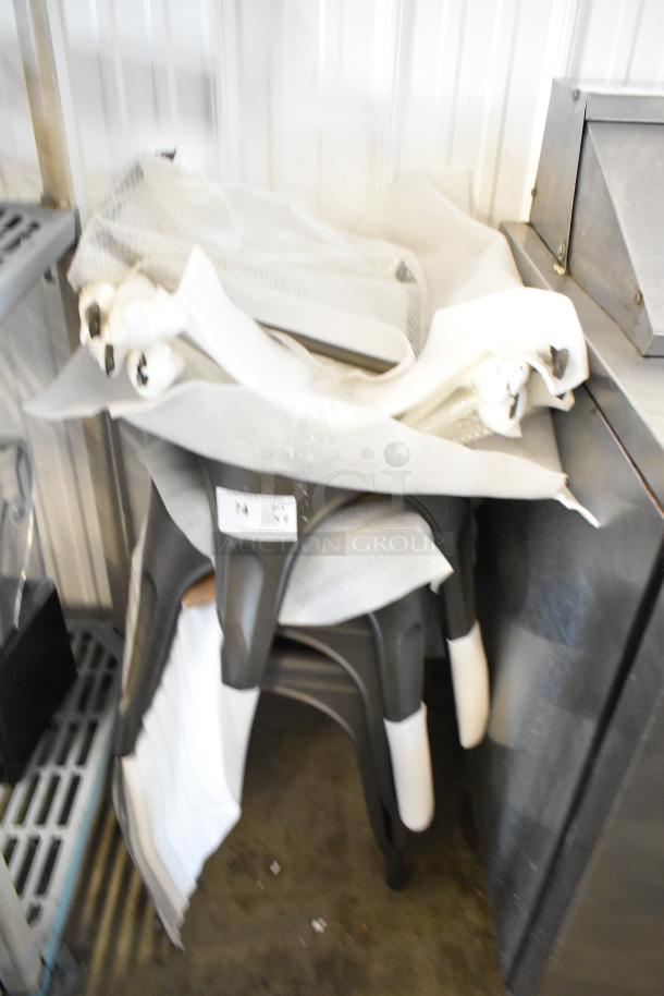 Four gray metal Tolix style stools in protective wrap, stacked. New condition, ideal for modern decor.