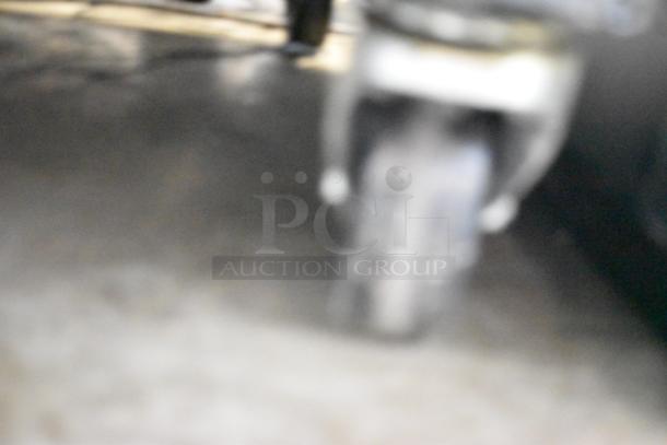 Blurry image of a wheel or caster, likely underneath an appliance. Difficult to discern specific details or condition.