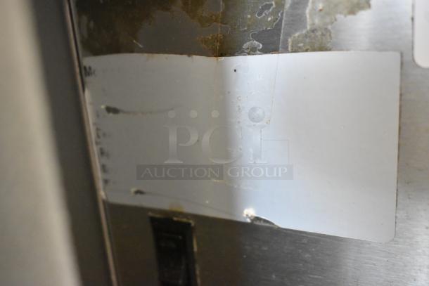 Stainless steel commercial deli display case, floor style, 115 volts, 1 phase. Visible wear and label residue on surface.