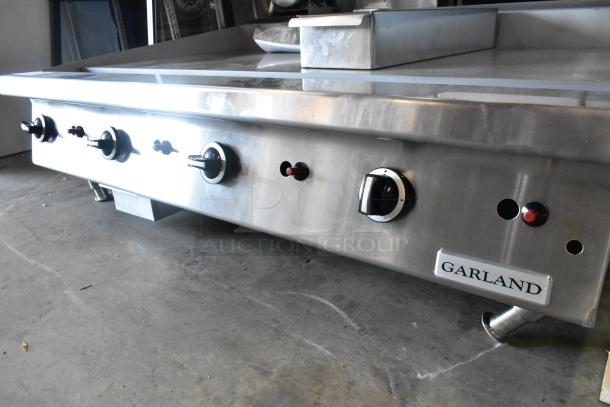 Garland stainless steel commercial gas flat top griddle, brand new with minor scratches. Features control knobs and brand label.