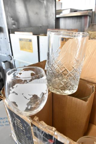 Box containing assorted glasses, including a wine glass with world map etching and a cut-crystal tumbler. In good condition.