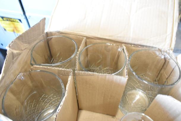 Box containing various clear glass tumblers with etched patterns, in cardboard packaging. Glasses appear in good condition.