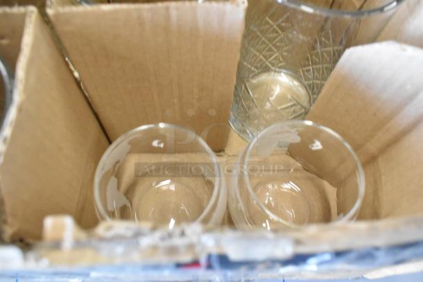Box of assorted drinking glasses with varying designs, including clear and textured patterns, in cardboard dividers.