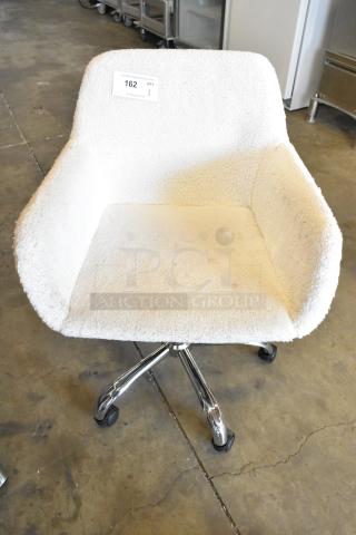 White chair on casters with a textured upholstery, metal frame, in used condition, numbered tag '162' attached.