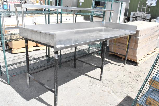 Stainless steel table with back splash and over shelf, industrial design, used condition, visible in outdoor setting.