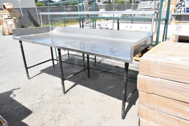 Stainless steel table with back splash and over shelf. Features black legs, used condition. Ideal for commercial settings.