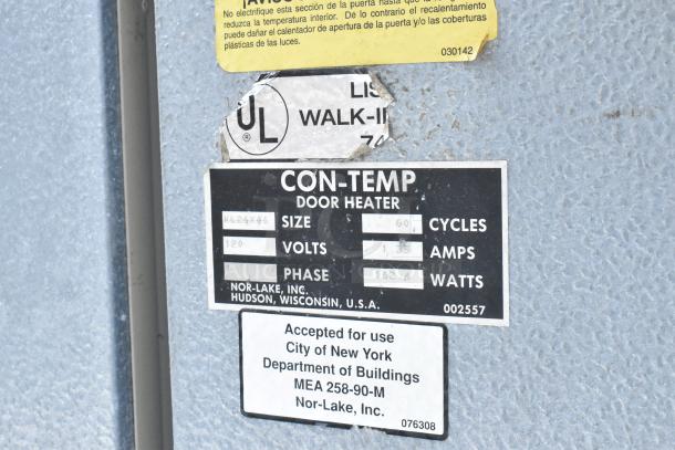 Norlake self-contained walk-in cooler box with compressor and condenser, featuring door heater label with voltage and watt details.