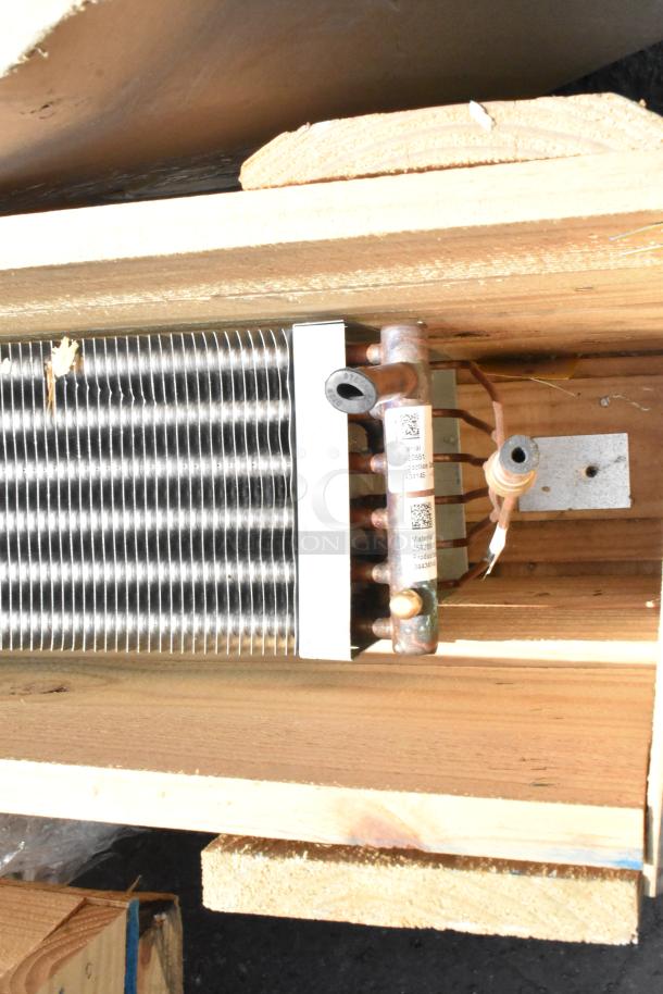Brand new evaporator coil in a wooden crate, showcasing metal fins and copper tubing. Labels indicate material details.