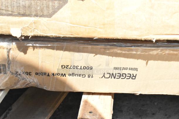 Cardboard box labeled "Regency" containing new scratch and dent 18-gauge work table, visible damage on edges.