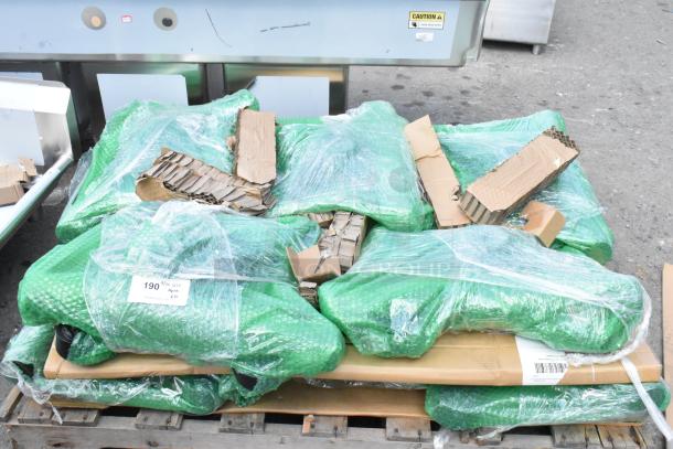 10 brand new scratch and dent items, including table leg base pieces, wrapped in green bubble wrap on a pallet.