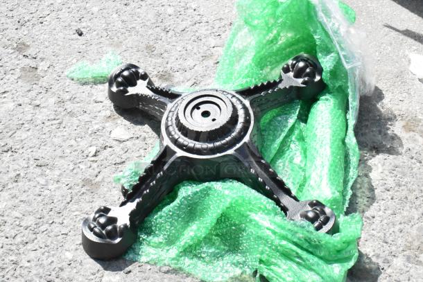Black cast iron table leg base piece on green bubble wrap, brand new, slight scratches visible, durable and functional design.