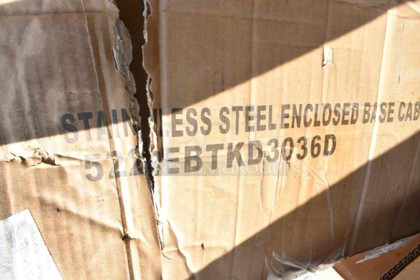 Torn cardboard box showing markings "Stainless Steel Enclosed Base Cabinet 522EBTKD3036D," indicating contents inside.