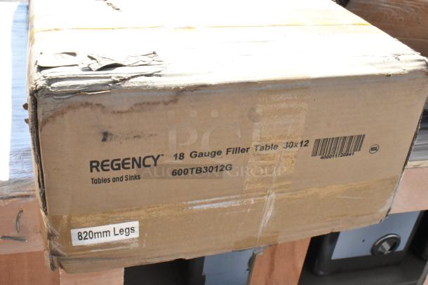 Box labeled Regency 18 Gauge Filler Table 30x12, model 600TB3012G, with barcode and "820mm Legs" marking. Condition: Scratch and Dent.
