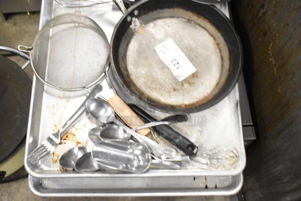 Lot of kitchen items including a worn skillet, silver utensils, a mesh strainer, and baking trays; tag reads "123".