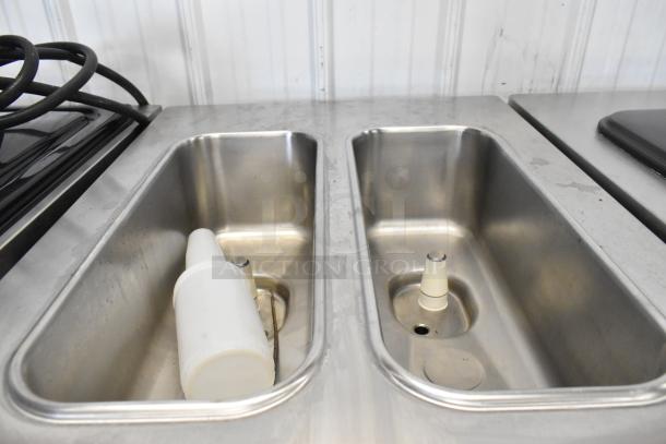 Stainless steel utility area with twin compartments and hoses.