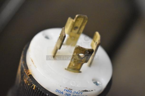 Close-up of a plug with visible markings "HBL2421" and "20A 3Ø 250V." The plug appears metal with slight surface wear.