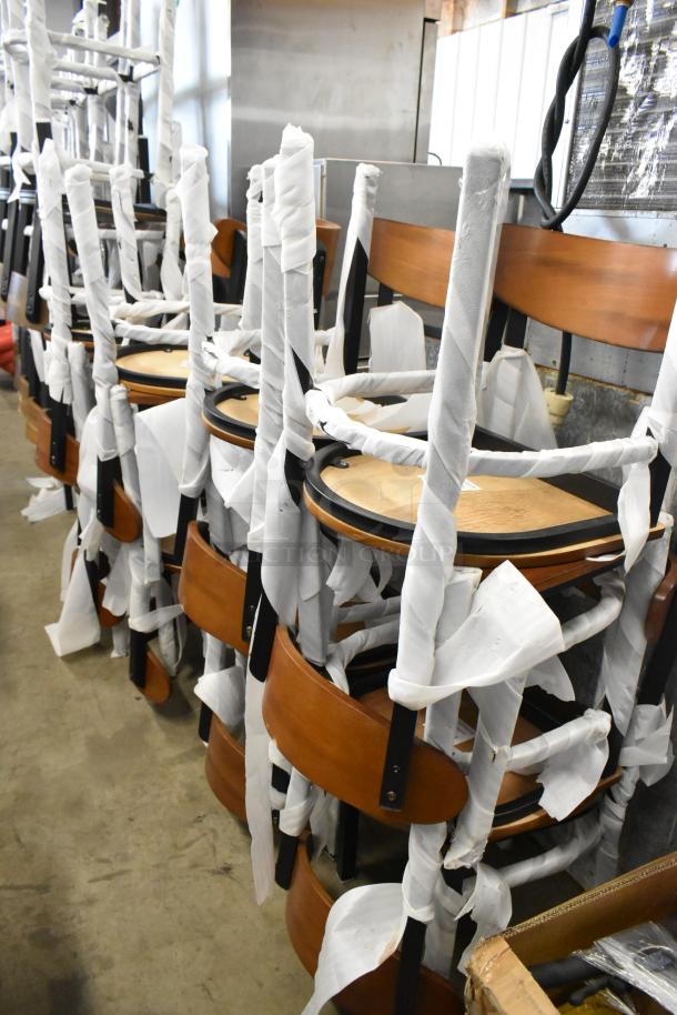 16 new Lancaster Table & Seating black metal dining chairs, wooden back and seat, partially wrapped, scratch and dent condition.