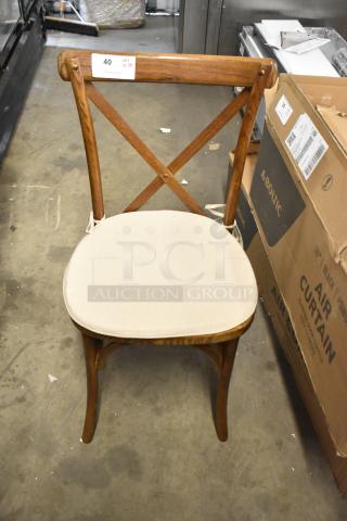 Brand new wooden dining chair with cross back, tan seat cushion. Scratch and dent condition. Quantity label: 18 available.
