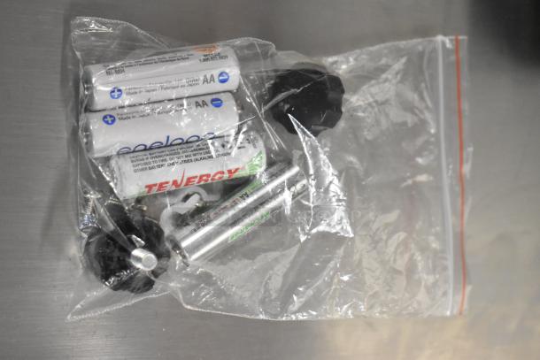 Transparent bag containing AA batteries and plastic knobs, likely accessories for the BRAND NEW AvaWeigh BS70 scale.