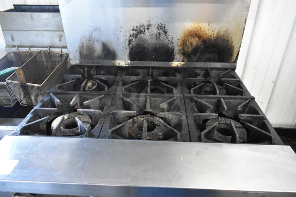 Bakers Pride stainless steel 6-burner gas range with oven, over shelf, and backsplash; showing signs of use; commercial setup.