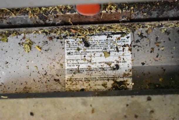 Close-up of the Bakers Pride range with visible grease and debris on a metal surface, showing maintenance instructions partial obscured.