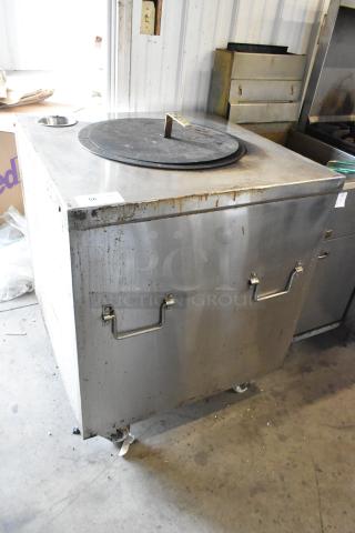 Stainless steel gas-powered tandoor oven on commercial casters. Floor style, some signs of use, sturdy handles visible.