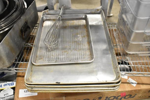 Assorted metal baking pans and poly containers in used condition, stacked on shelves, with a wire whisk on top.