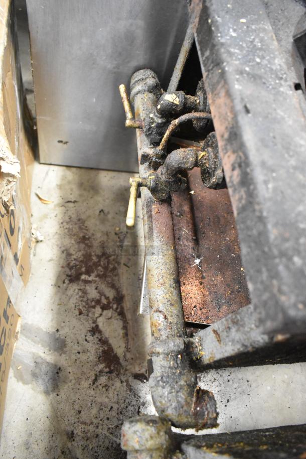 Metal commercial gas-powered single burner stock pot range, used with visible rust and wear, showing gas pipe fittings and control.