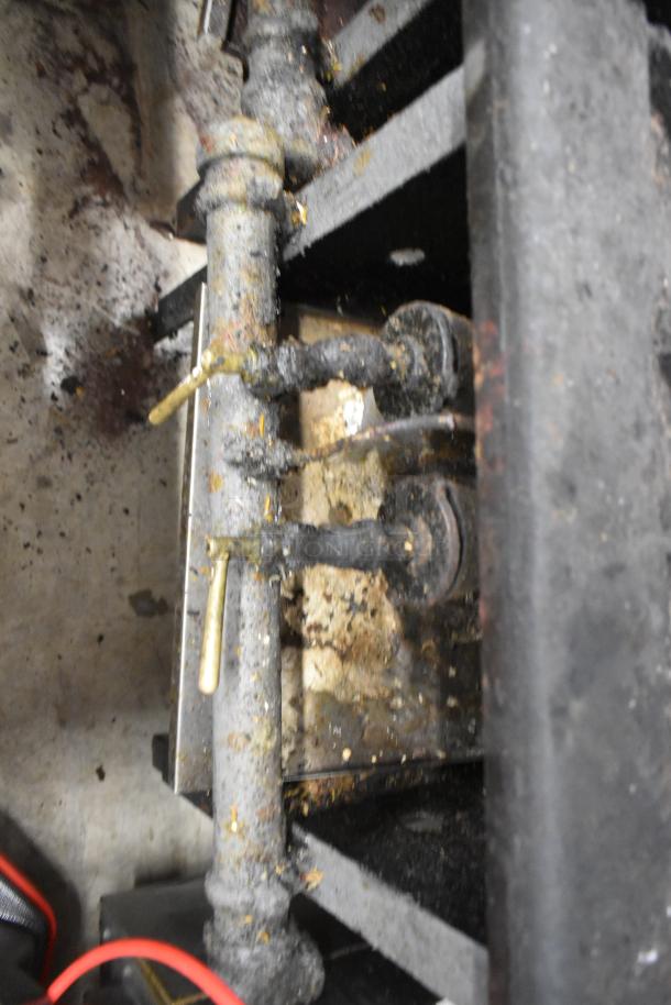 Metal commercial gas-powered single burner stock pot range, showing wear and residue, includes visible control knobs and pipes.
