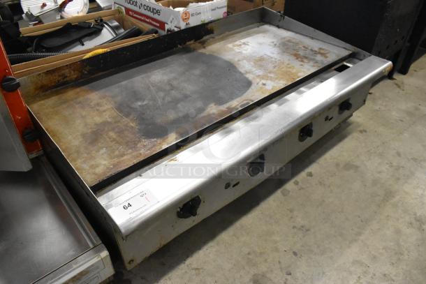 Stainless steel commercial countertop gas griddle with four control knobs, visible wear on cooking surface, auction tag showing item 64.
