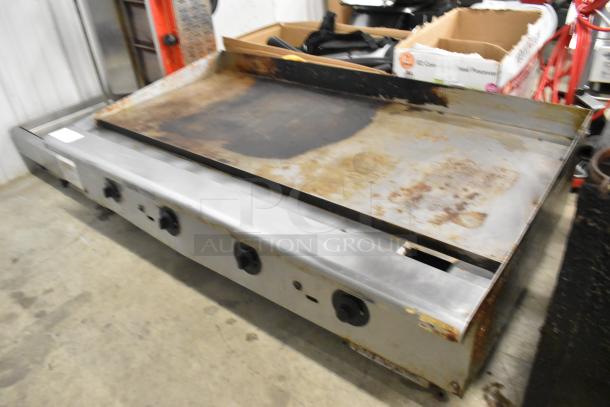 Stainless steel commercial countertop gas griddle with flat top, exhibits signs of wear, featuring multiple control knobs.