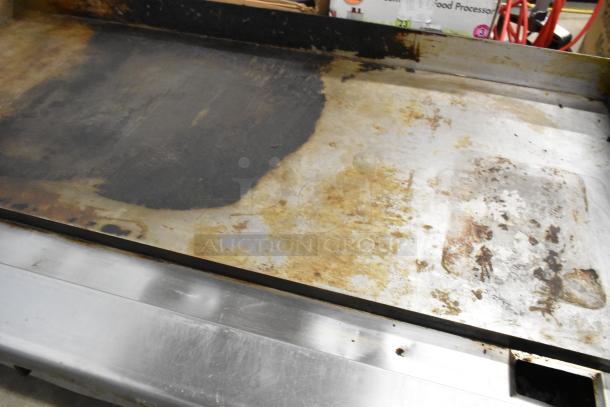 Stainless steel commercial countertop gas griddle with visible wear and discoloration on cooking surface.