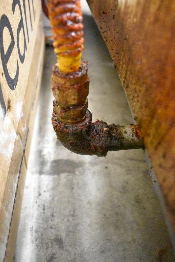A rusted connection on a gas line under a commercial countertop griddle, showing wear and corrosion.