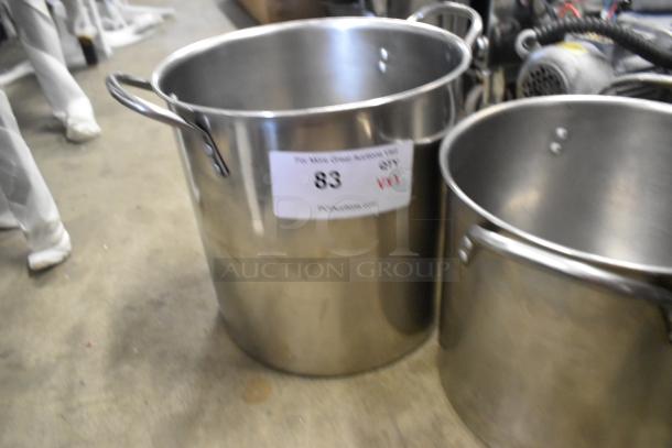 Three metal stock pots with handles, featuring an auction label "83". Pots appear in used condition, placed on a concrete floor.
