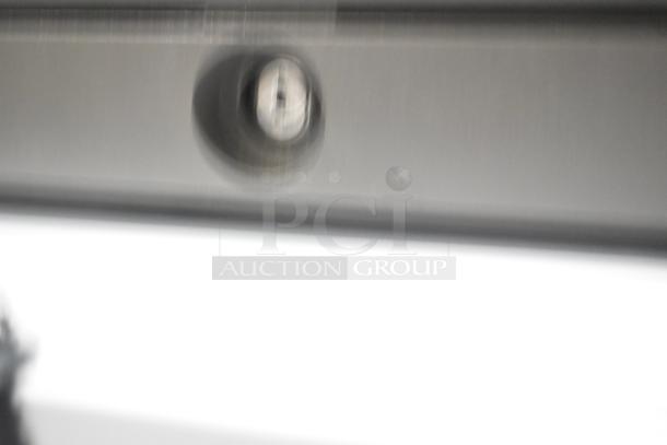 Blurry image of a gray metal cash drawer with a visible key lock mechanism.