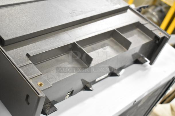 Gray metal cash drawer with multiple compartments, visible screws, and a latch mechanism. In used condition.