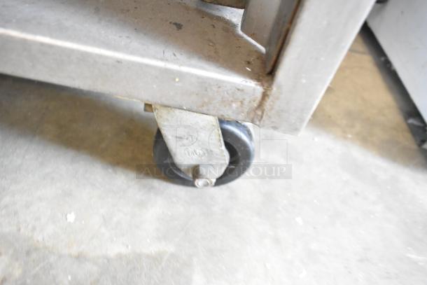 Baxter stainless steel commercial oven caster, showing metal frame and wheel, part of a rotating rack oven on casters.