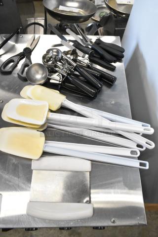 Lot of various kitchen utensils including scrapers, dishers, scissors, and spatulas, all in good condition on metal surface.